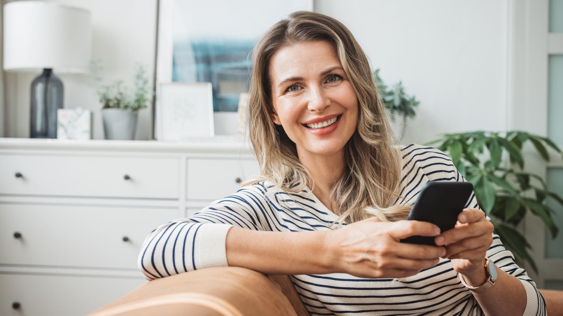 Ženska se smehlja med uporabo telefona, kar izraža občutek veselja in vključenosti v njeno dejavnost