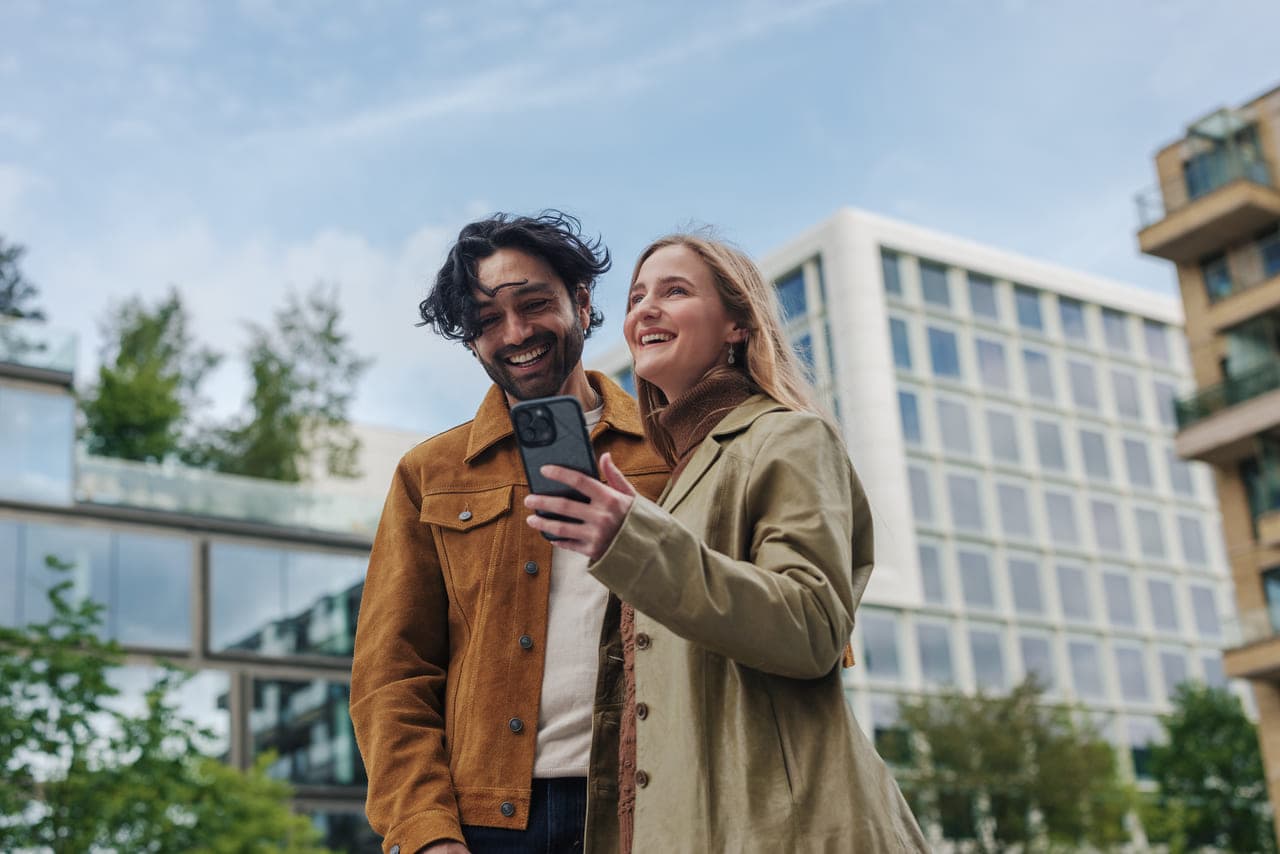 Moški in ženska se nasmejita, medtem ko si v moderini stavbi pred njimi naredita selfie